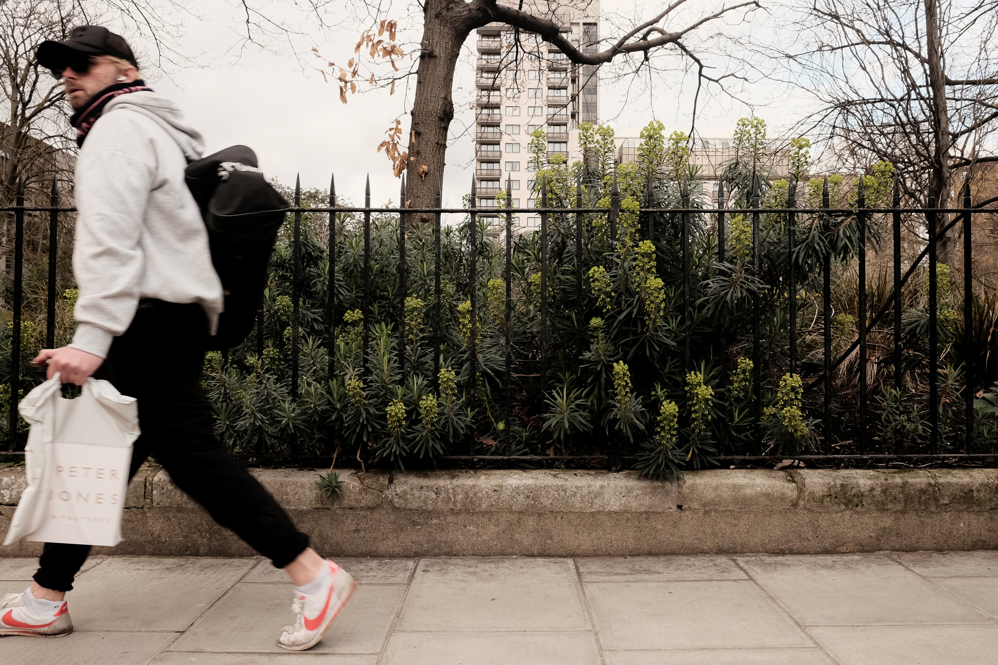 Black park fence with a londoner walking by in Nike shoes