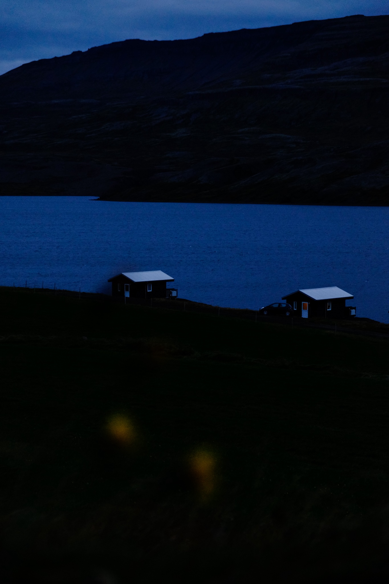 Two small cottages on a farm with a lake in the distance followed by a mountainside