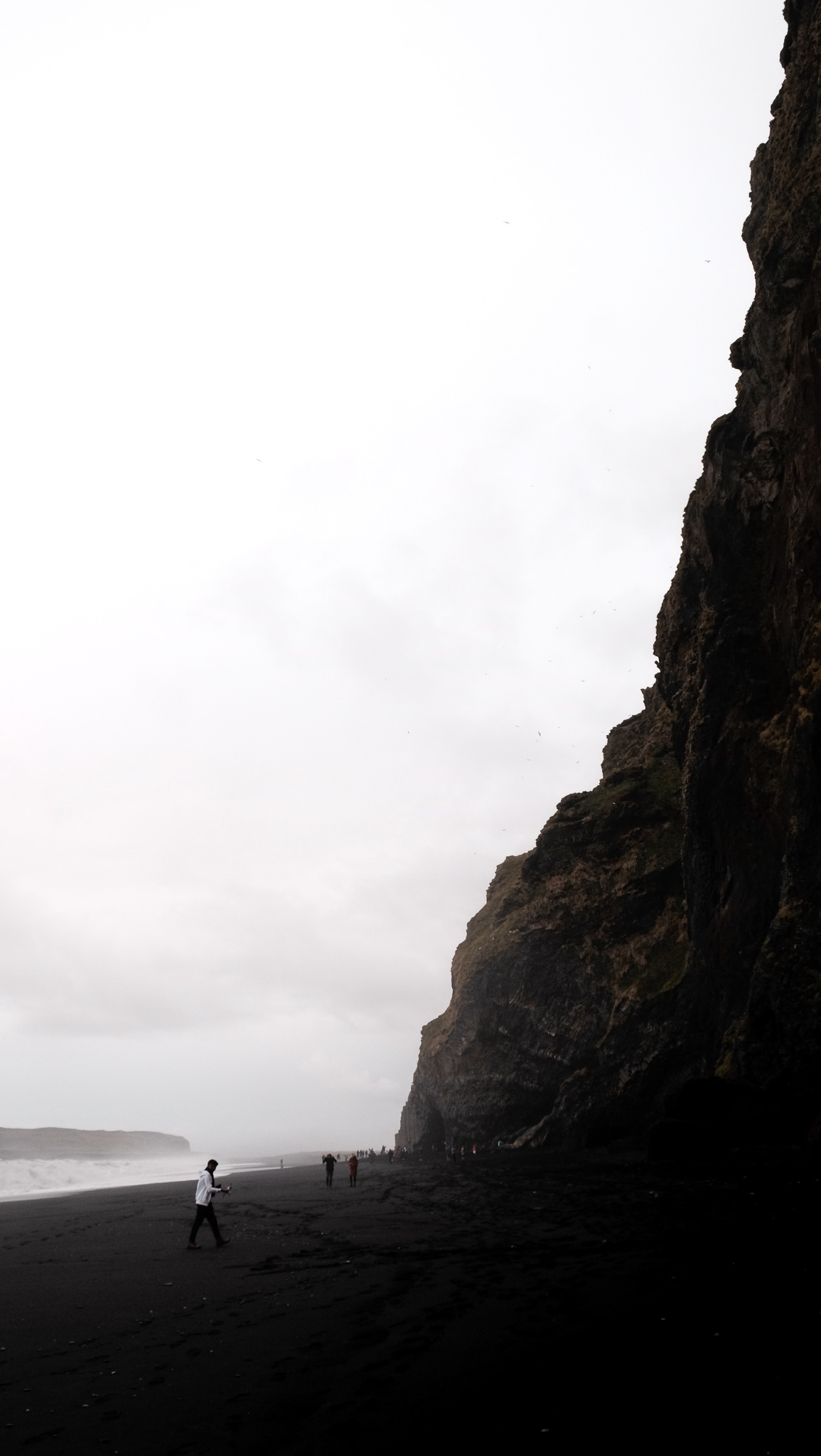 Photo down the black beach showing the stark contrast of the white sky against the black sand and black mountain side