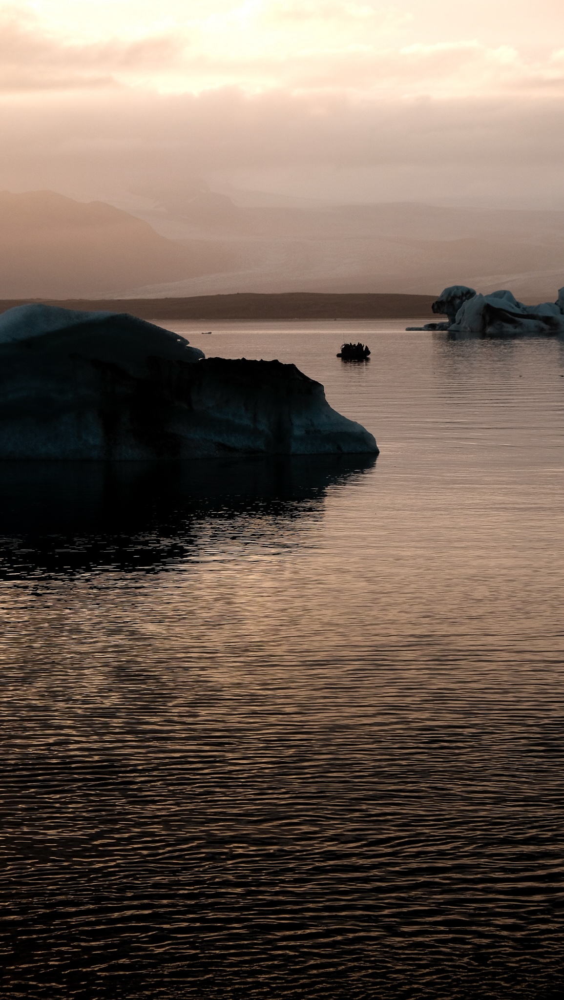 A boat in the distance makes it's way through the glaciel lake avoiding icebergs