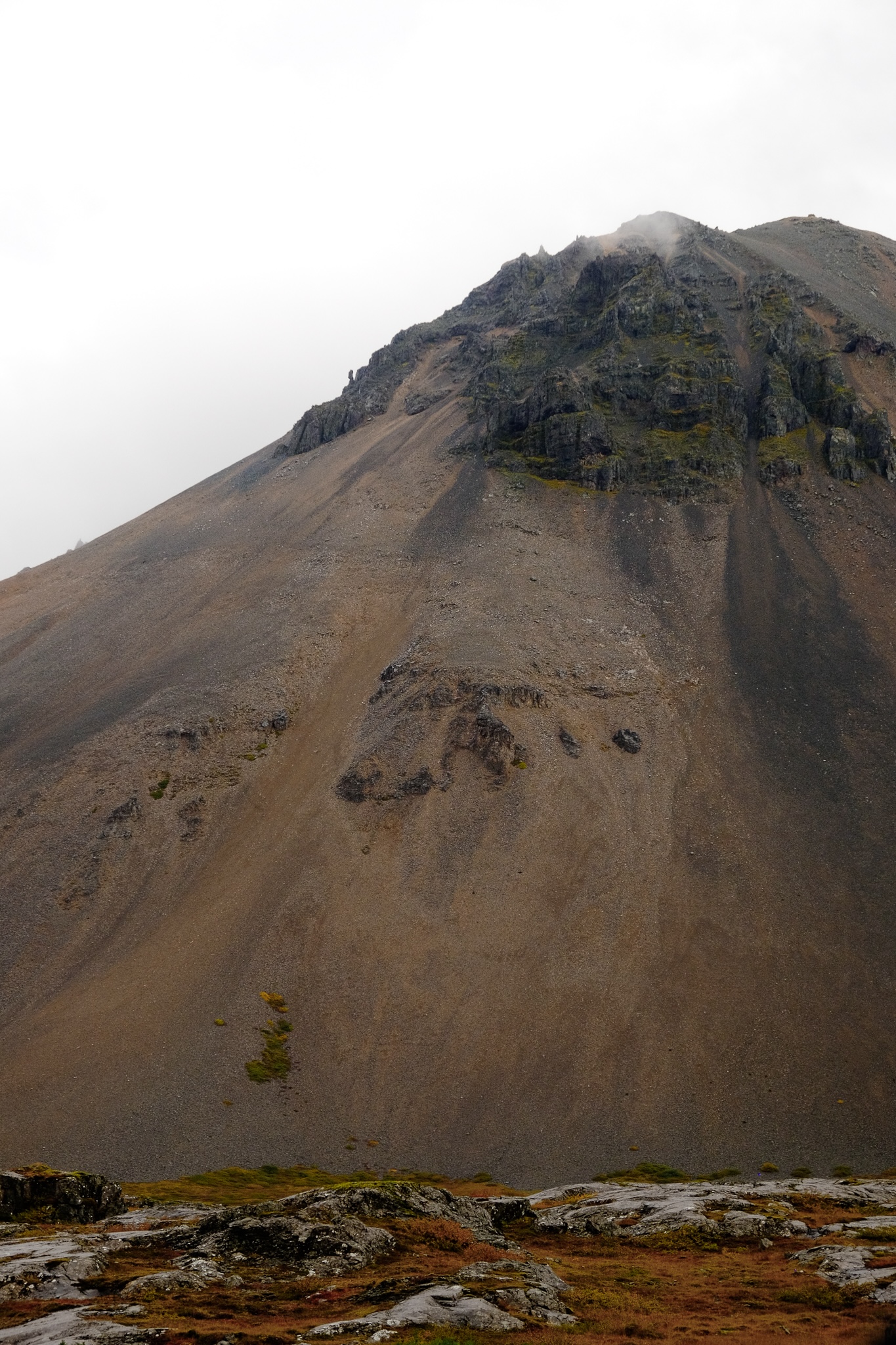 Brown sand and black rock mountain is imposing against white rock with grass growing between the rocks