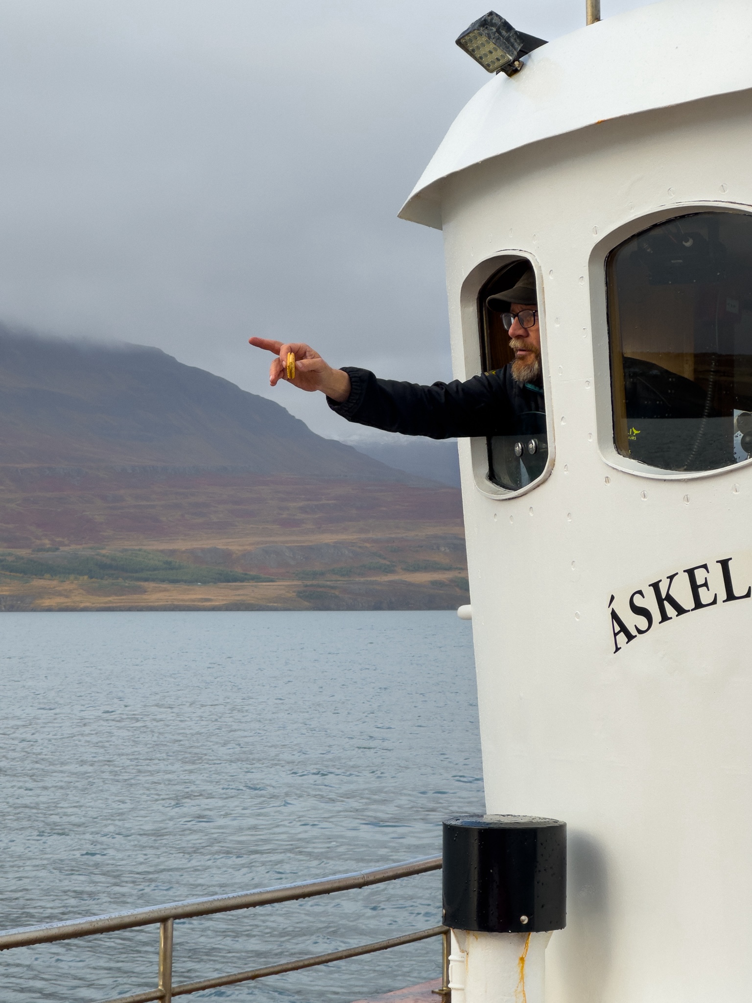 Captain pointing to a whale sighting from the cockpit, a half eaten cheap-looking biscuit in the hand he's using to point