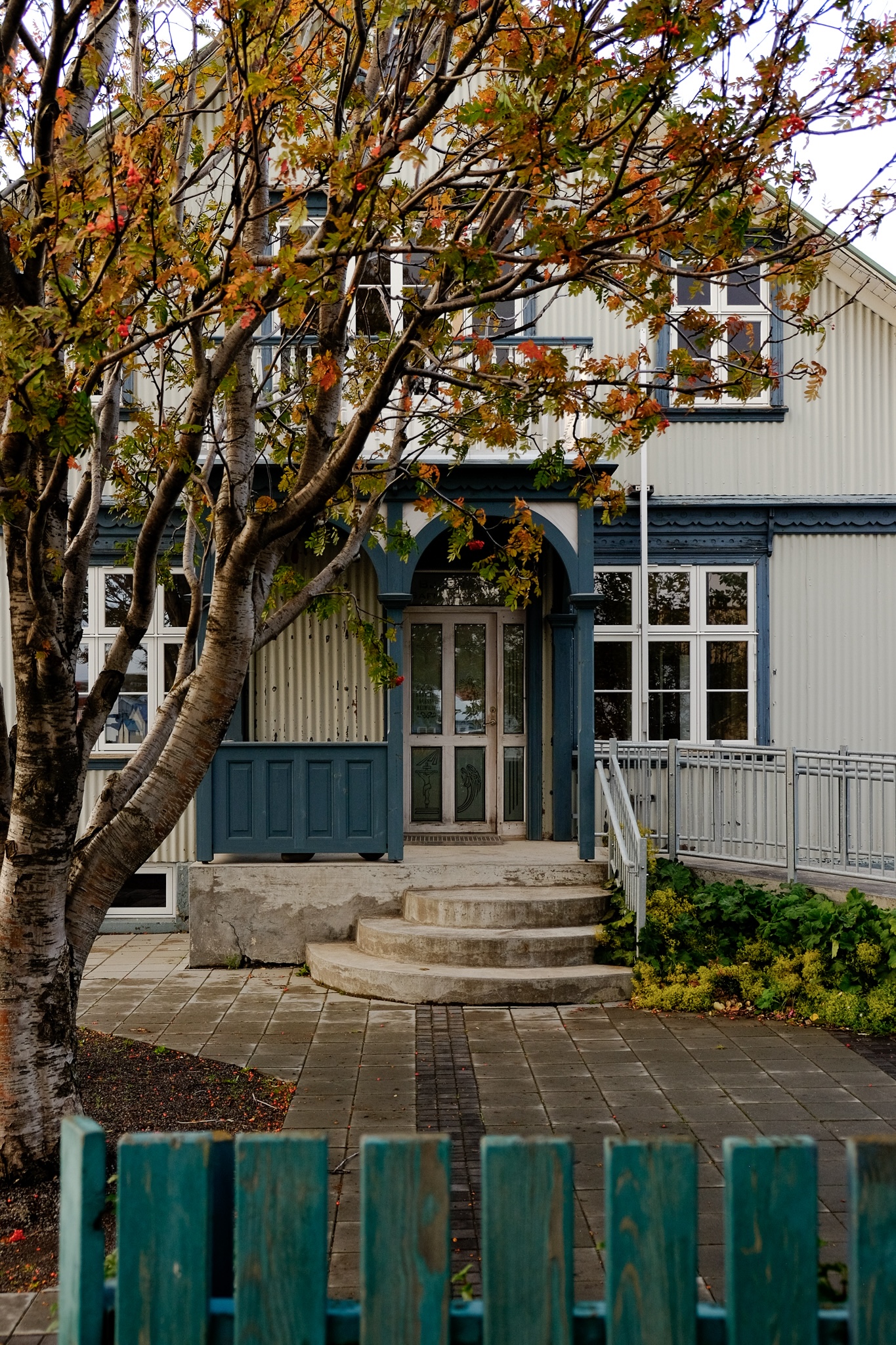A white corrugated building with faded blue trim in Husavik in Iceland with a turqoise wooden picket fence