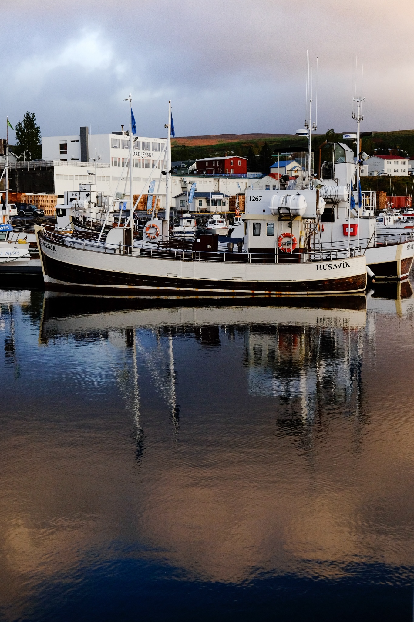 Boat and it's reflection in colourful water of the harbour from the reflection of the sunset's colours effect on the clouds in the sky