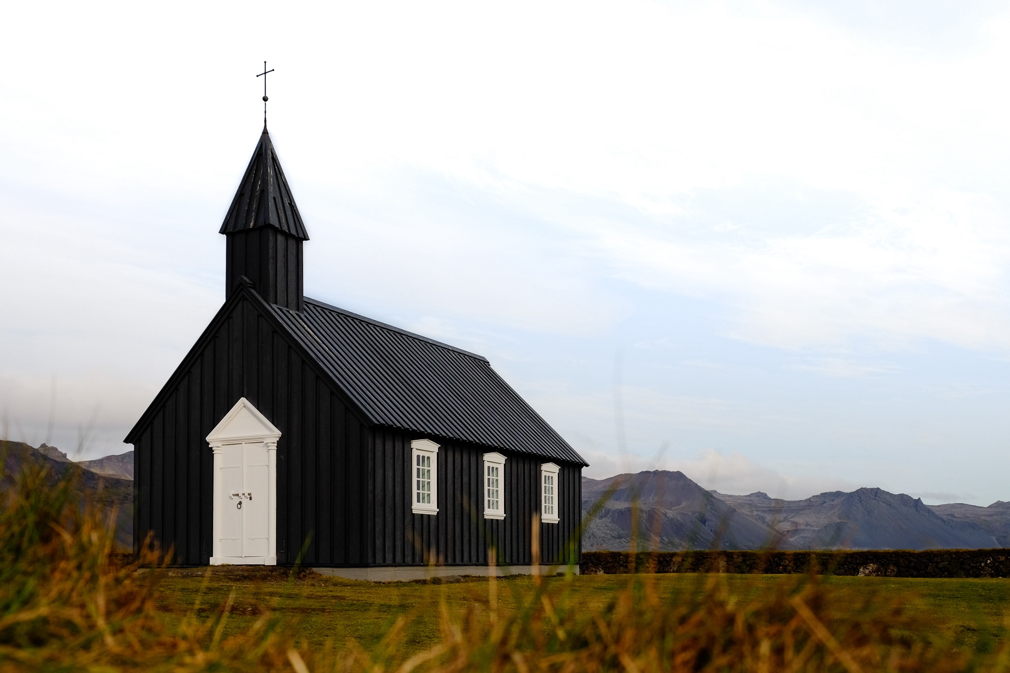 A black church of wooden panelled walls and roof with starkly contrasting white window frames and door