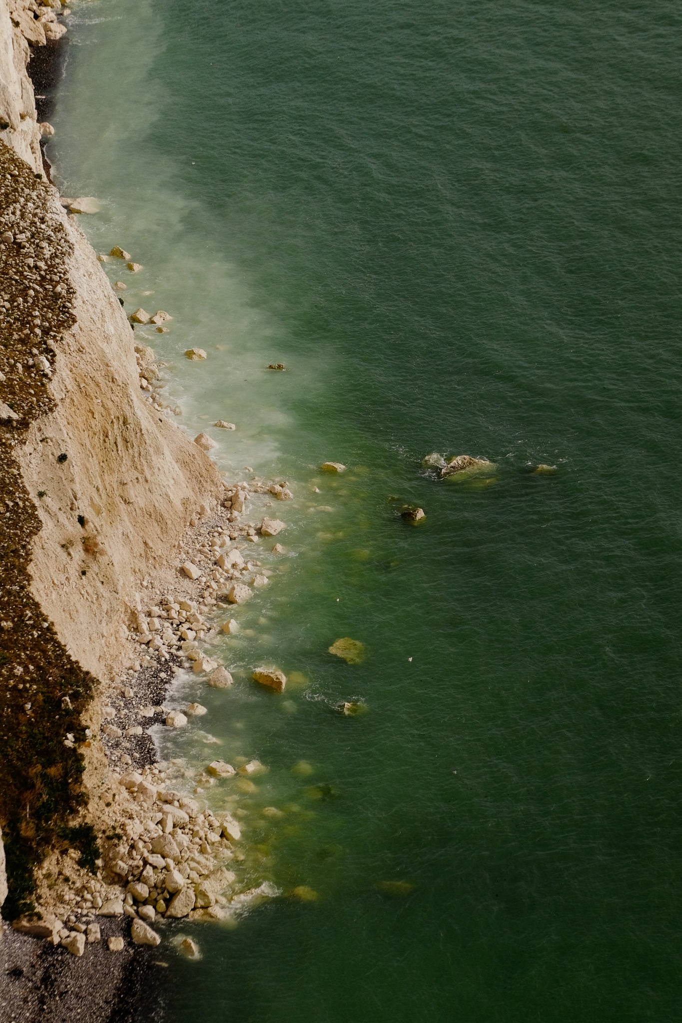 From the cliffs down to the sea shore green-turquoise water creates a gradient of colour from the ocean to the shore of black pebbles and white rocks coming off the cliffs.