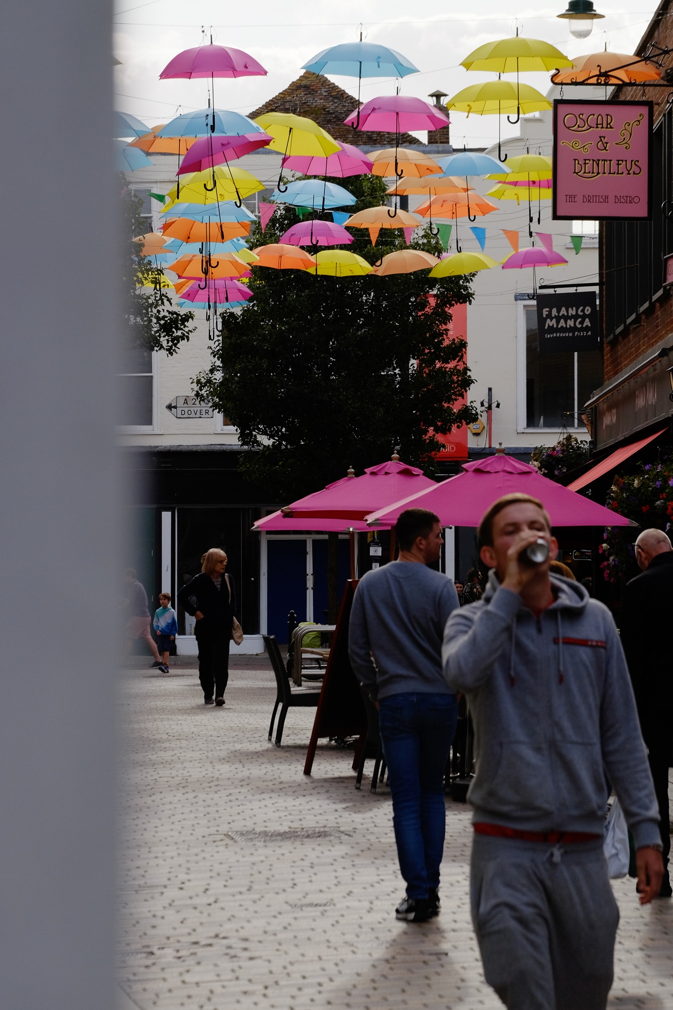A canopy of colourful umbrella's strung across a walking path in Canterbury in pink, blue, yellow, and orange.