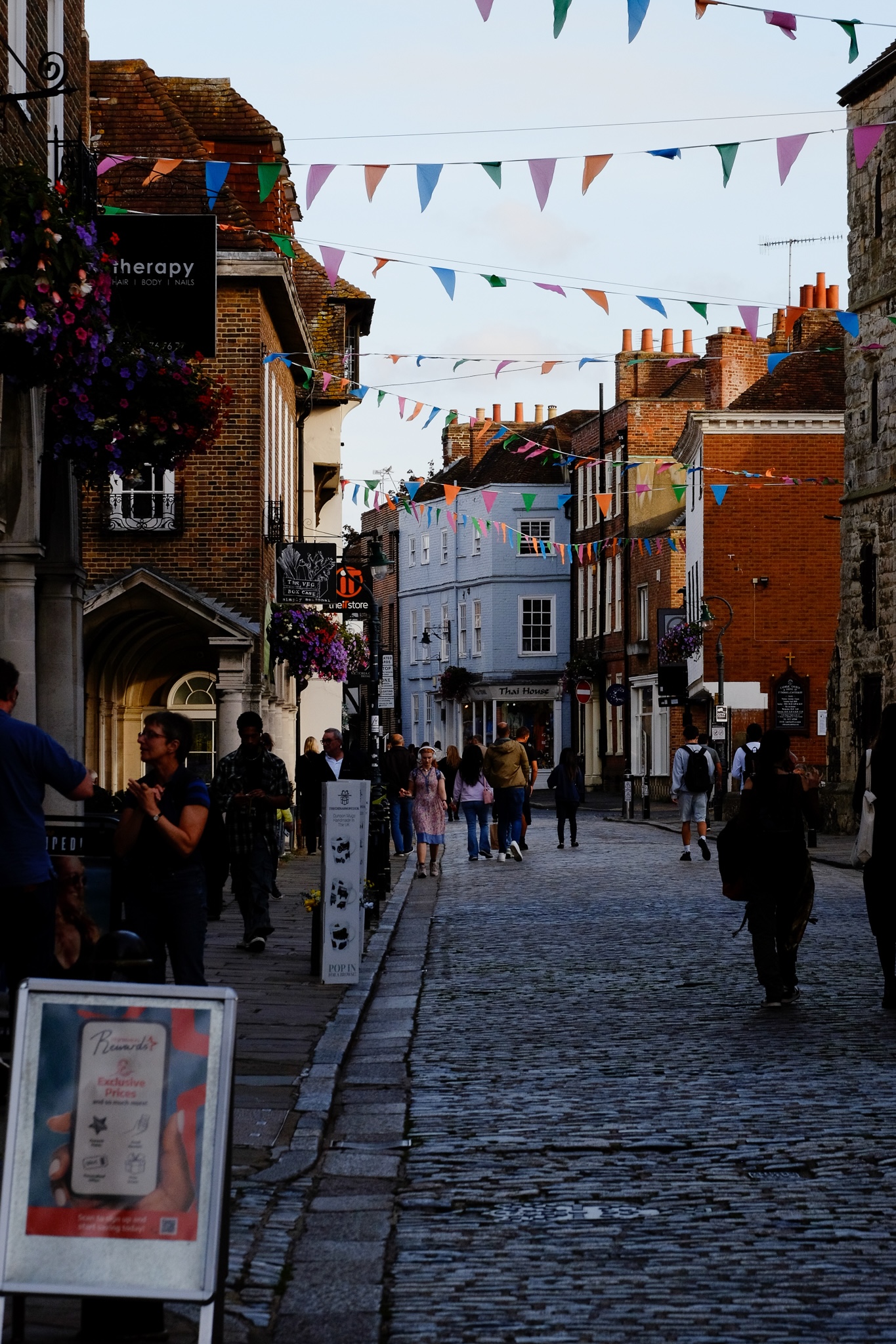Colourful triangular flag bunting strung zig-zag across a cobble street in Canterbury