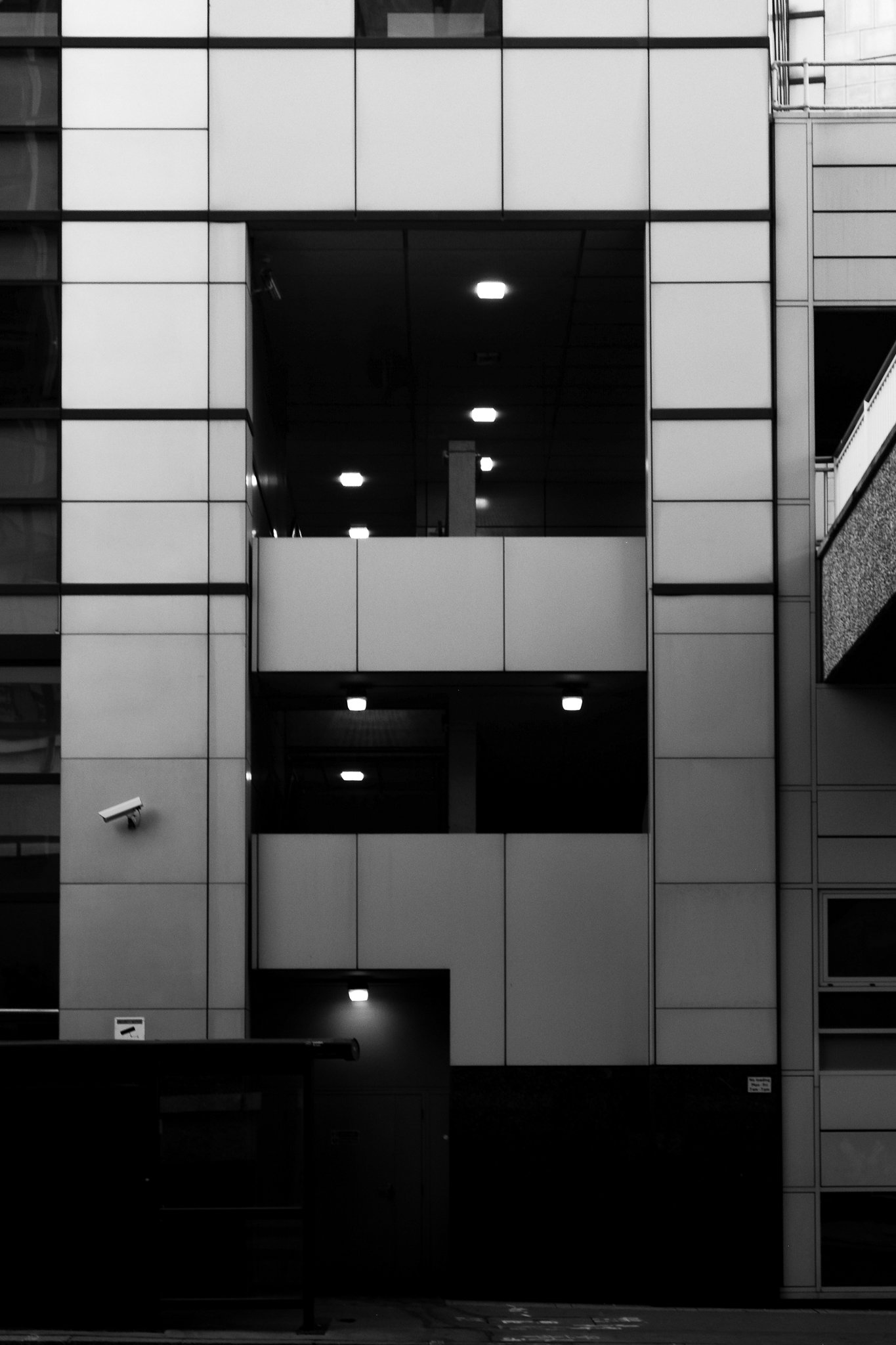 Black and white image flat on of a staircase from outside of the building, the staircase lights shining in the darkness.