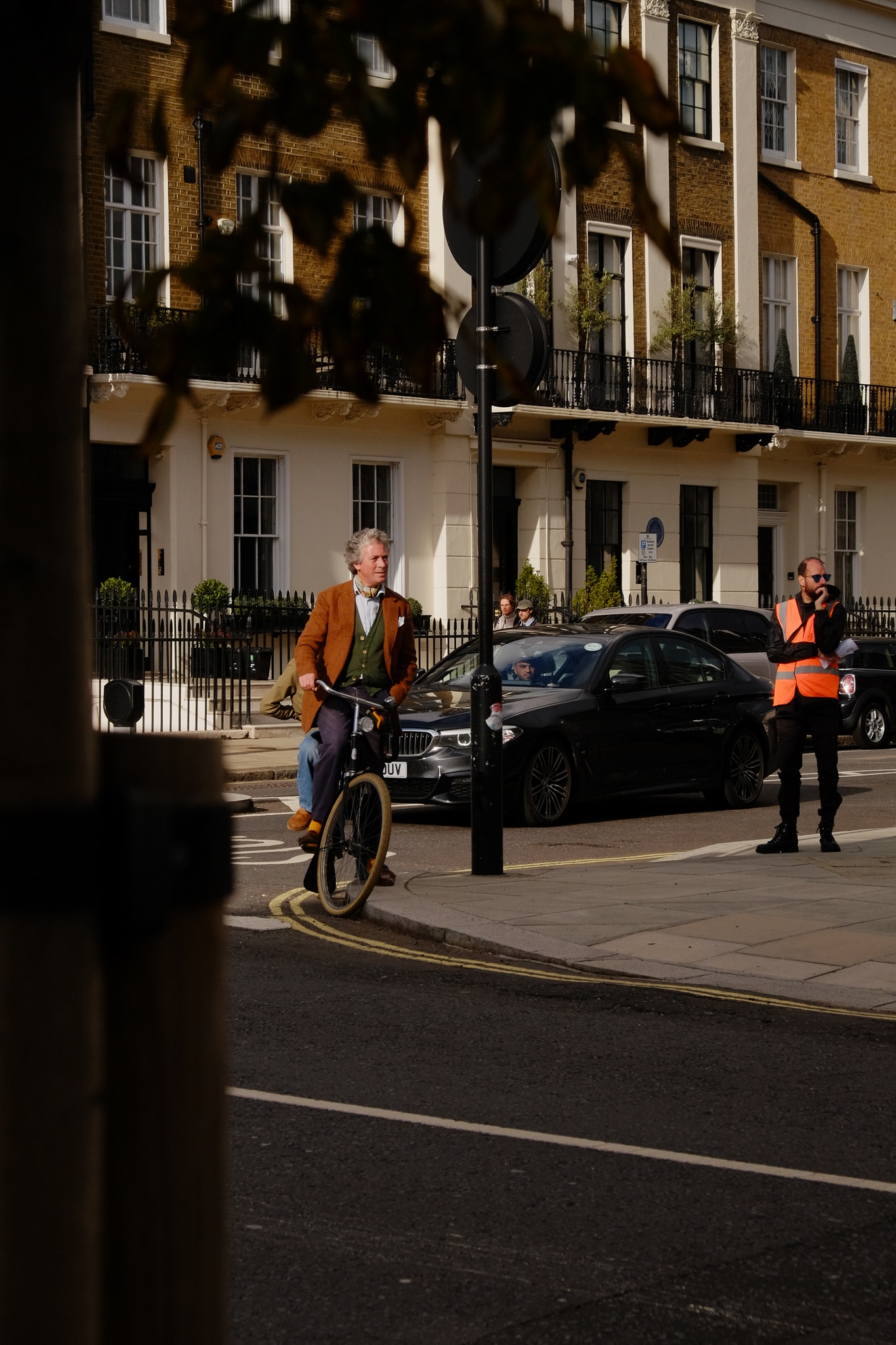 Dapper man and women on a tandem bike looking down the street, in the background are yellowbrick houses with white trim and black steel balconies