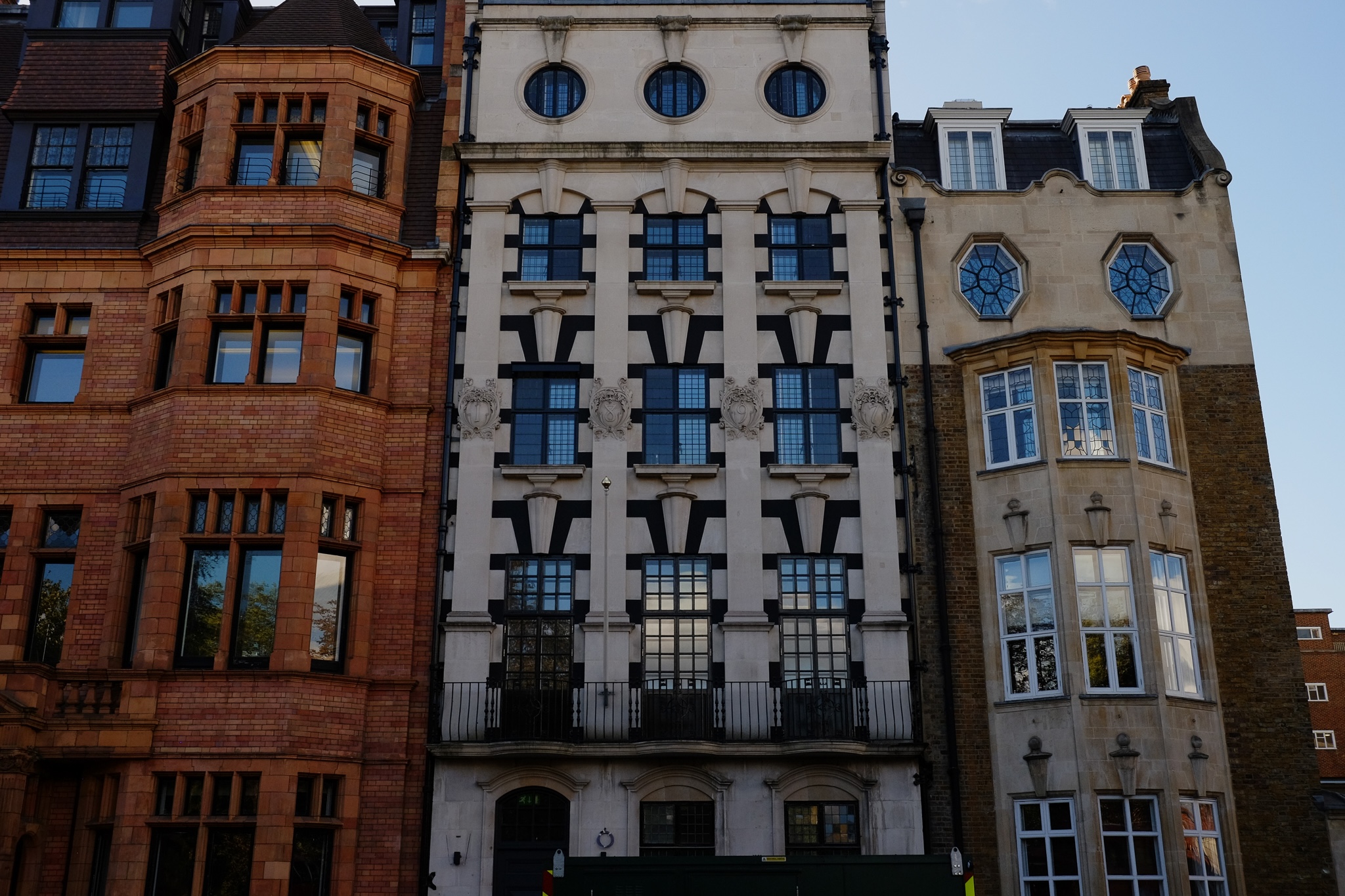 Three ornate buildings head on with different architecture styles and building materials, one red brick, one white concrete with black trim, and one brown concrete and brown brick.