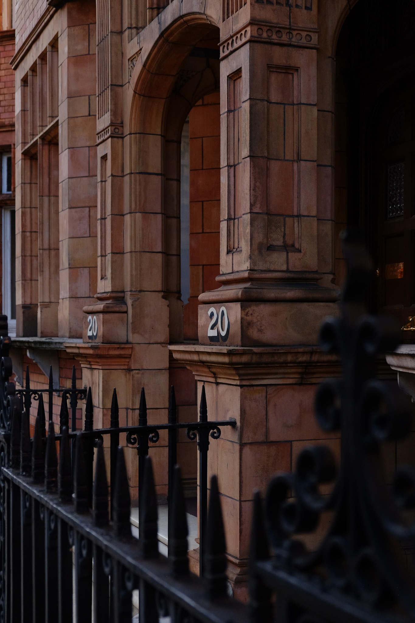 Faded red brick building entrance with black gate and two tone number 20 painted on the arch entrance
