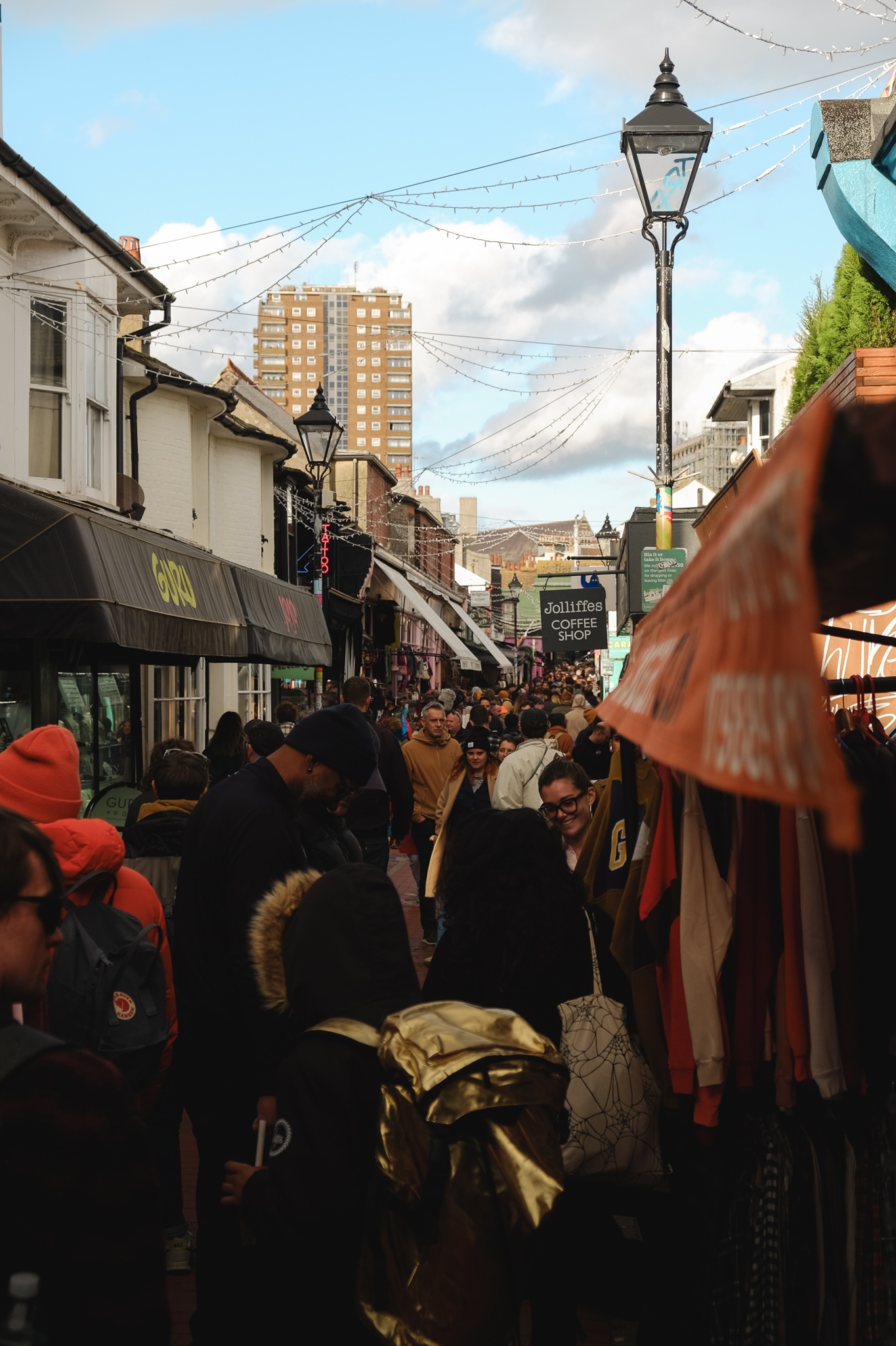 A busy corridor street packed with people and lined with interesting shops on either side of the street
