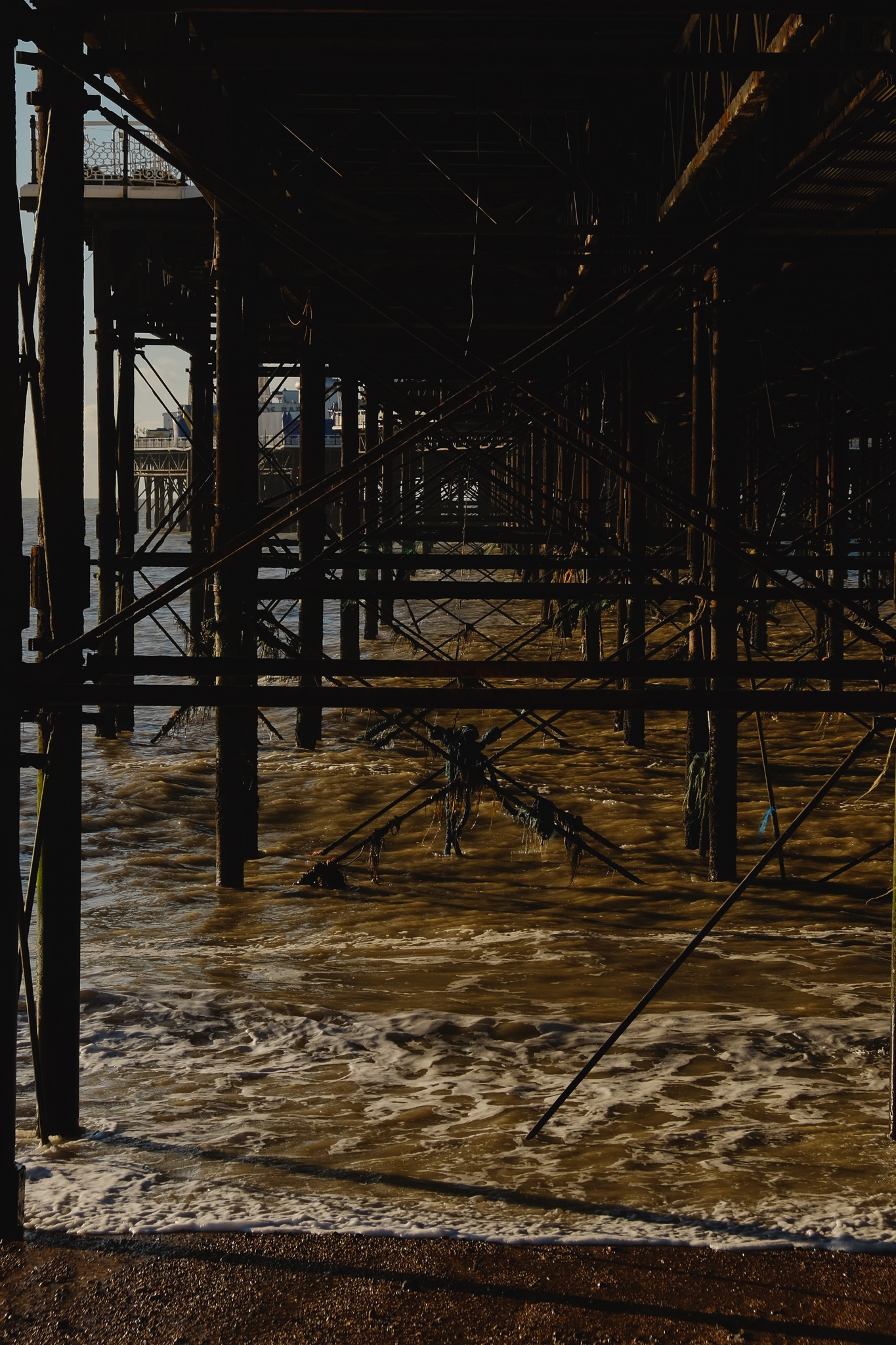 A repeated pattern created from the pier support structure, a web of pylons from the pier go into the ocean, with waves crashing underneath, it's really dirty